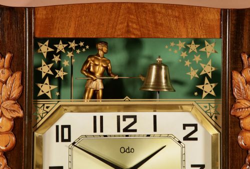 fig 3. An Art Deco carved walnut wall clock by Odo featuring a brass automaton bell striker and a Venetian glass lower window.