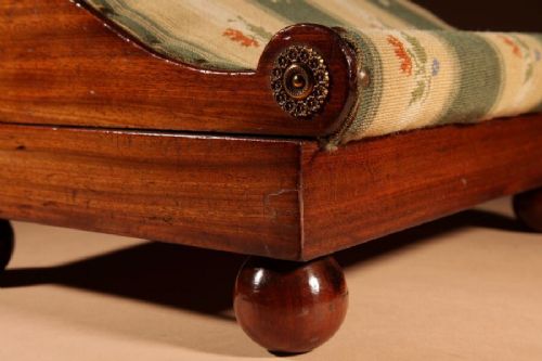 A 19th-century Continental mahogany sloped footstool featuring striped floral upholstery, brass side rosettes, and turned bun feet. View V