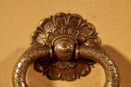 An 18th-century cast bronze door knocker featuring a stylized dolphin design suspended from a decorative floral rosette backplate. View II