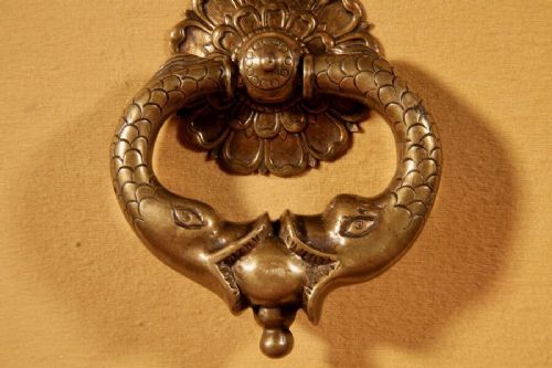 An 18th-century cast bronze door knocker featuring a stylized dolphin design suspended from a decorative floral rosette backplate. View III
