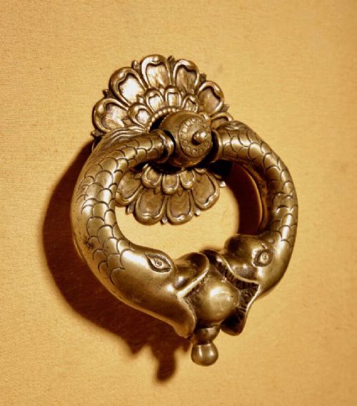 An 18th-century cast bronze door knocker featuring a stylized dolphin design suspended from a decorative floral rosette backplate. View IV