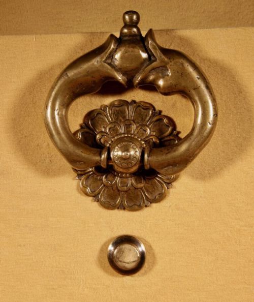 An 18th-century cast bronze door knocker featuring a stylized dolphin design suspended from a decorative floral rosette backplate. View V