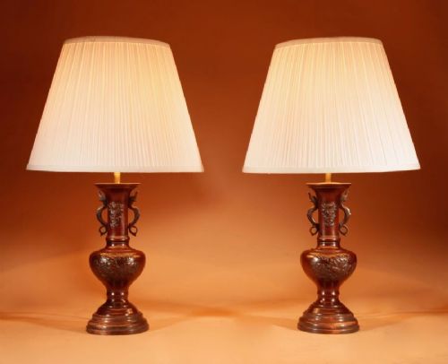 fig 1. A pair of dark Japanese bronze baluster vase lamps featuring relief carvings and fitted cream pleated shades.