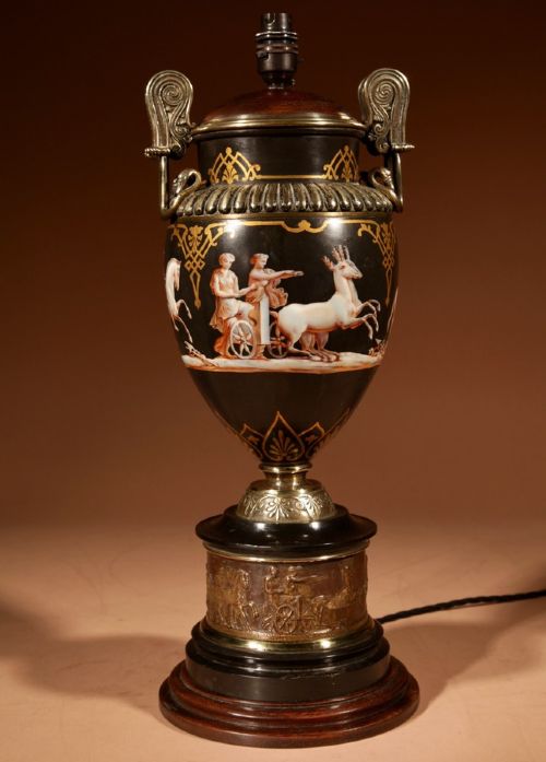 fig 1. A 19th-century Grand Tour table lamp featuring a black ceramic urn base with red-figure chariot artwork, gilt bronze handles, and a pleated conical fabric shade.