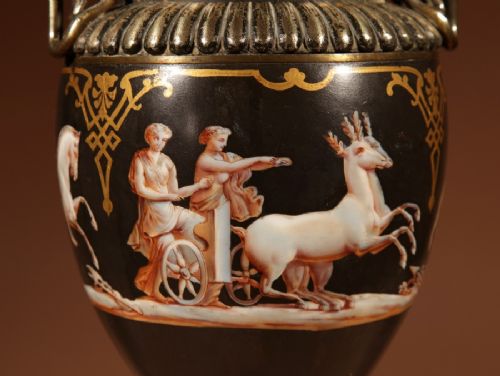 fig 2. A 19th-century Grand Tour table lamp featuring a black ceramic urn base with red-figure chariot artwork, gilt bronze handles, and a pleated conical fabric shade.