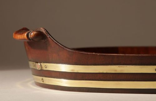 An oval mahogany serving tray featuring staved wood construction, twin carved side handles, and two horizontal brass bands securing the outer rim. View IV