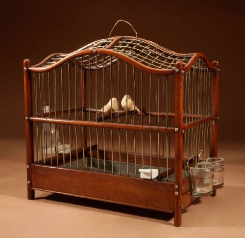 fig 1. An Anglo-Dutch mahogany and brass birdcage featuring an arched wire dome roof, slide-out drawer tray, wooden perches, and accompanying glass vessels.