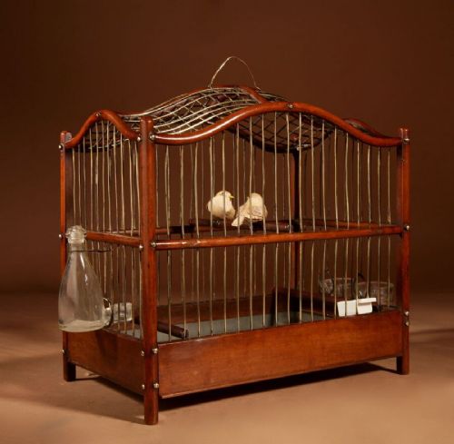 An Anglo-Dutch mahogany and brass birdcage featuring an arched wire dome roof, slide-out drawer tray, wooden perches, and accompanying glass vessels. View IV