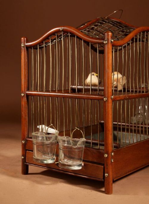 An Anglo-Dutch mahogany and brass birdcage featuring an arched wire dome roof, slide-out drawer tray, wooden perches, and accompanying glass vessels. View VII