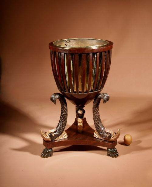 fig 1. A French Empire mahogany slatted wine cooler featuring a brass liner and supported by three carved ebonised dolphin legs on a triform base with paw feet.