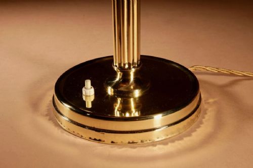 An Art Deco brass table lamp with a reeded column base and a tan stitched leather shade featuring geometric cut-outs and fringe trim. View IV