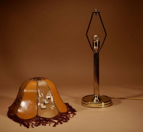 An Art Deco brass table lamp with a reeded column base and a tan stitched leather shade featuring geometric cut-outs and fringe trim. View VII