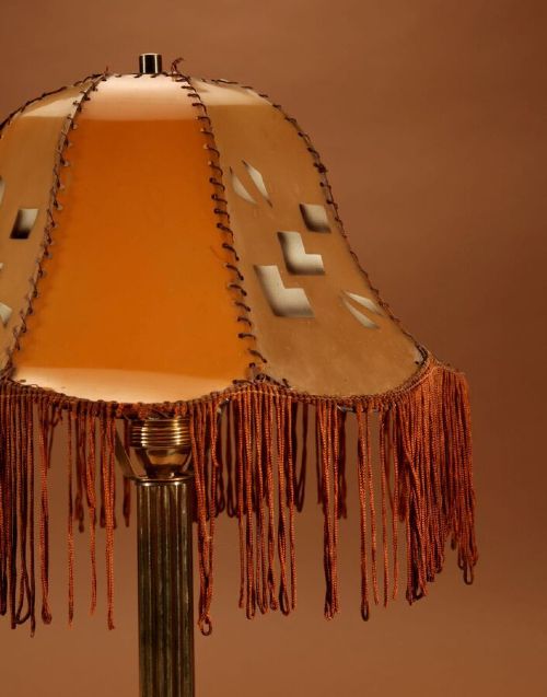 An Art Deco brass table lamp with a reeded column base and a tan stitched leather shade featuring geometric cut-outs and fringe trim. View VIII