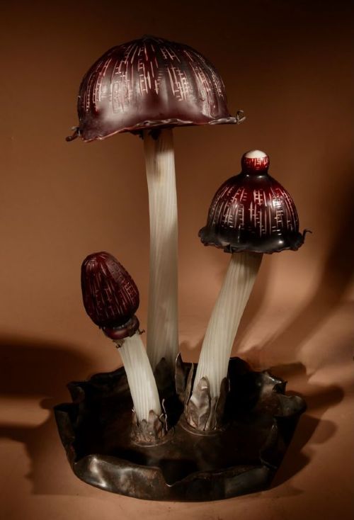 A triple mushroom table lamp featuring three illuminated white glass stems topped with red patterned glass caps set into a dark wrought iron base. View VIII