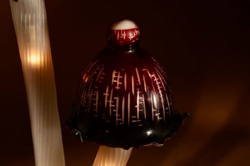 A triple mushroom table lamp featuring three illuminated white glass stems topped with red patterned glass caps set into a dark wrought iron base. View IX