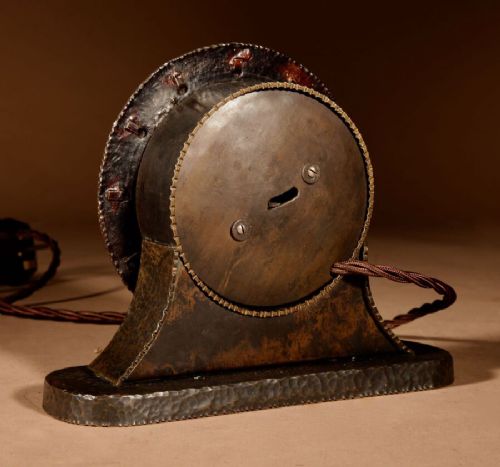 fig 1. A circular hand-hammered patinated brass electric clock on a flared base with rectangular brass hour markers.