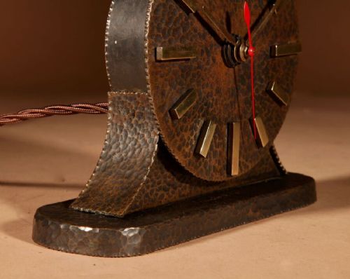 A circular hand-hammered patinated brass electric clock on a flared base with rectangular brass hour markers. View V