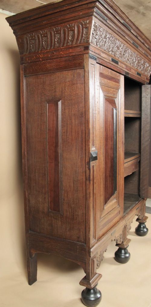 A Dutch Baroque oak armoire featuring two doors with raised geometric cushion panels, rosewood and ebony inlays, a carved frieze, and ebonised ball feet. View V