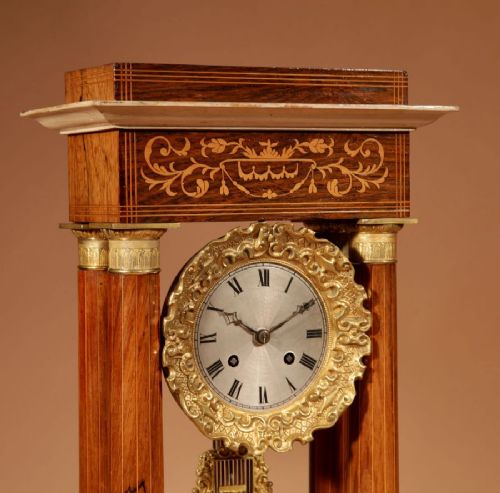 fig 2. A French Louis Philippe portico mantel clock set featuring floral wood inlay, architectural columns, a gilt metal pendulum, and two matching urn side pieces on decorative pedestals.