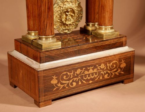 A French Louis Philippe portico mantel clock set featuring floral wood inlay, architectural columns, a gilt metal pendulum, and two matching urn side pieces on decorative pedestals. View V