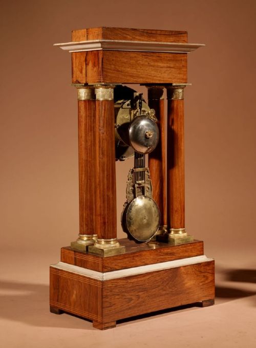 A French Louis Philippe portico mantel clock set featuring floral wood inlay, architectural columns, a gilt metal pendulum, and two matching urn side pieces on decorative pedestals. View VII