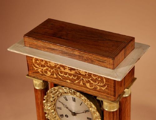 A French Louis Philippe portico mantel clock set featuring floral wood inlay, architectural columns, a gilt metal pendulum, and two matching urn side pieces on decorative pedestals. View VIII
