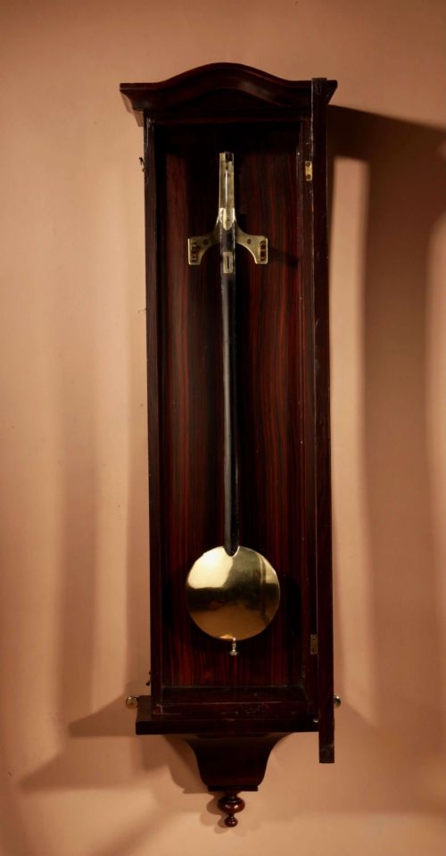 fig 1. An antique dark wood Vienna regulator wall clock featuring a glazed case, white enamel dial with Roman numerals, and a polished brass pendulum.