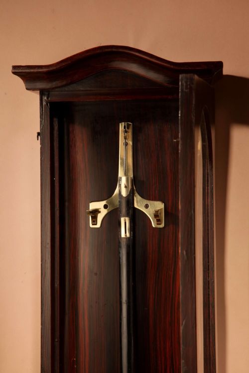 fig 2. An antique dark wood Vienna regulator wall clock featuring a glazed case, white enamel dial with Roman numerals, and a polished brass pendulum.