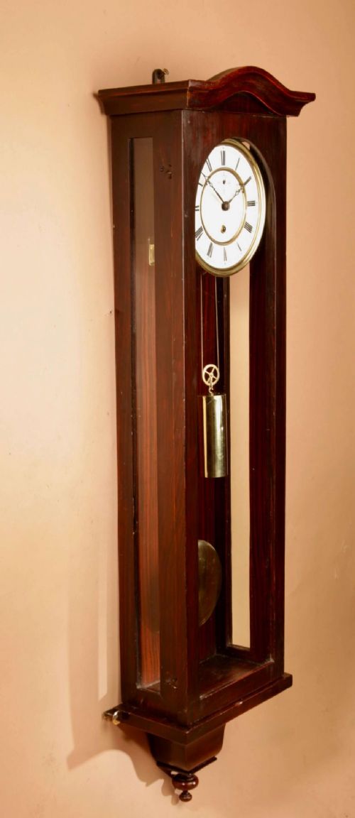 An antique dark wood Vienna regulator wall clock featuring a glazed case, white enamel dial with Roman numerals, and a polished brass pendulum. View VII