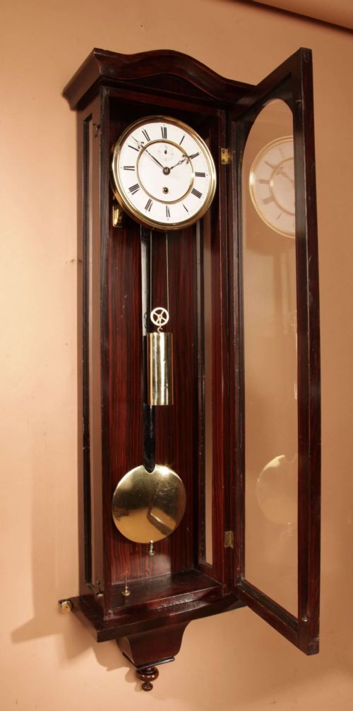 An antique dark wood Vienna regulator wall clock featuring a glazed case, white enamel dial with Roman numerals, and a polished brass pendulum. View VIII
