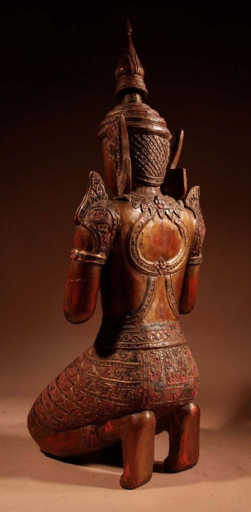 A carved wooden Thai Thepphanom guardian statue depicted kneeling with hands held in a prayer gesture, featuring a conical headdress and gilded red lacquered details. View XI