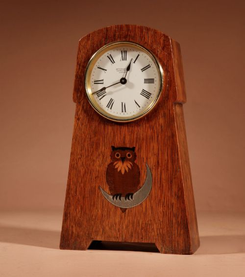 fig 1. An Arts and Crafts tapered oak mantel clock featuring a white circular dial and wood inlay depicting an owl perched on a pewter crescent moon.