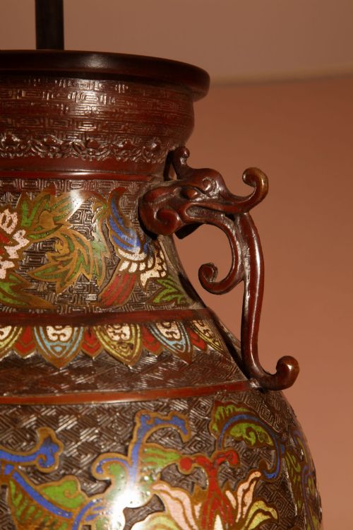 fig 1. A Japanese champleve bronze vase lamp with ornate scroll handles and polychrome enamel detailing, topped with a pleated white shade.