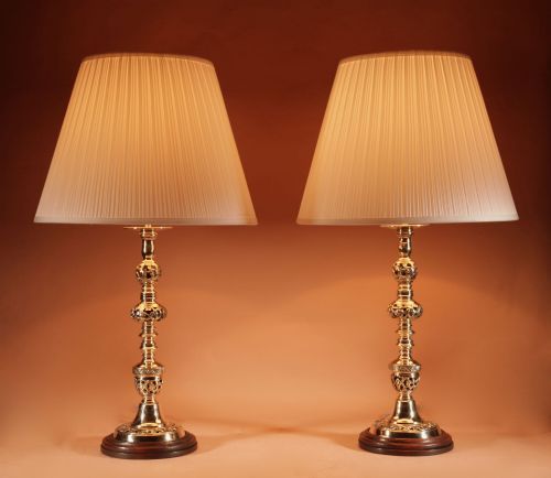 fig 1. A pair of turned brass table lamps featuring openwork cast detailing and cream pleated shades set against a neutral background.
