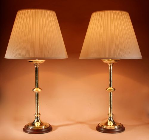 fig 1. A pair of polished brass table lamps featuring knopped stems, circular timber bases, and cream pleated shades.