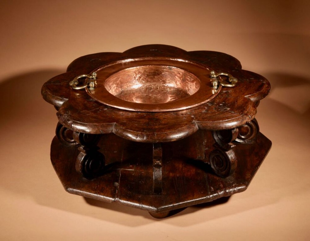 A low carved dark wood Spanish brasero featuring a scalloped rim and a central hammered copper insert with brass drop handles.