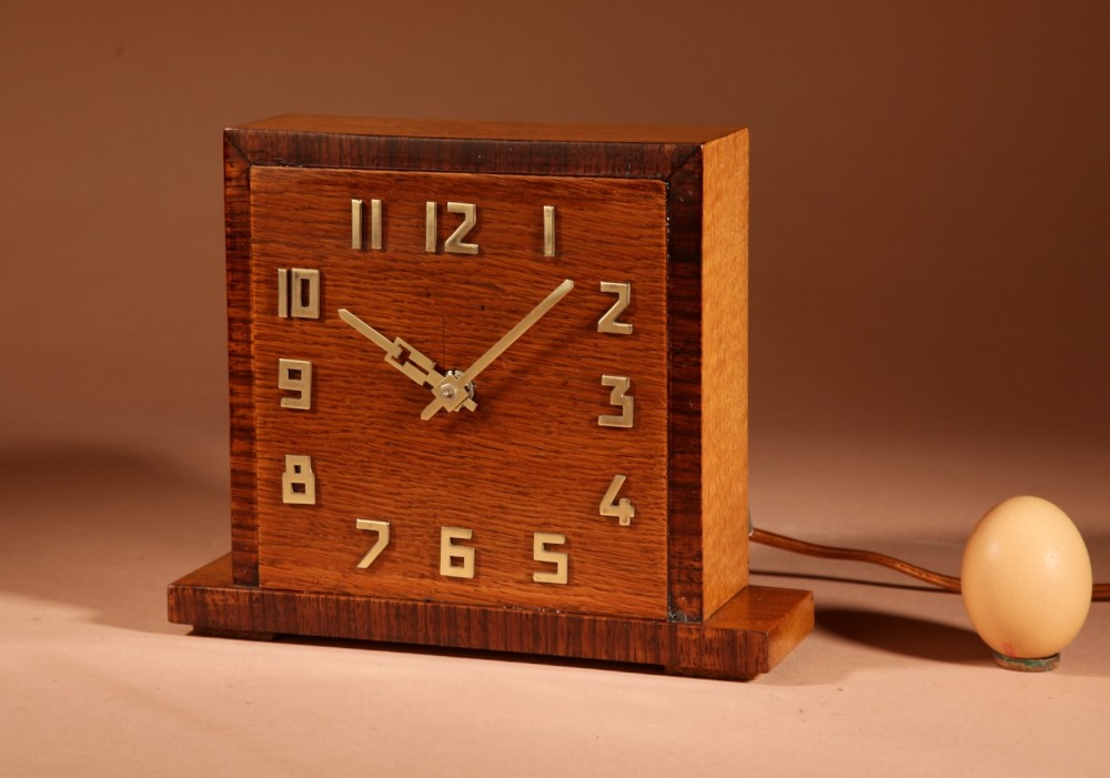 An Art Deco square oak mantel clock featuring a dark rosewood border frame, polished brass numerals, and an extended rectangular plinth base.