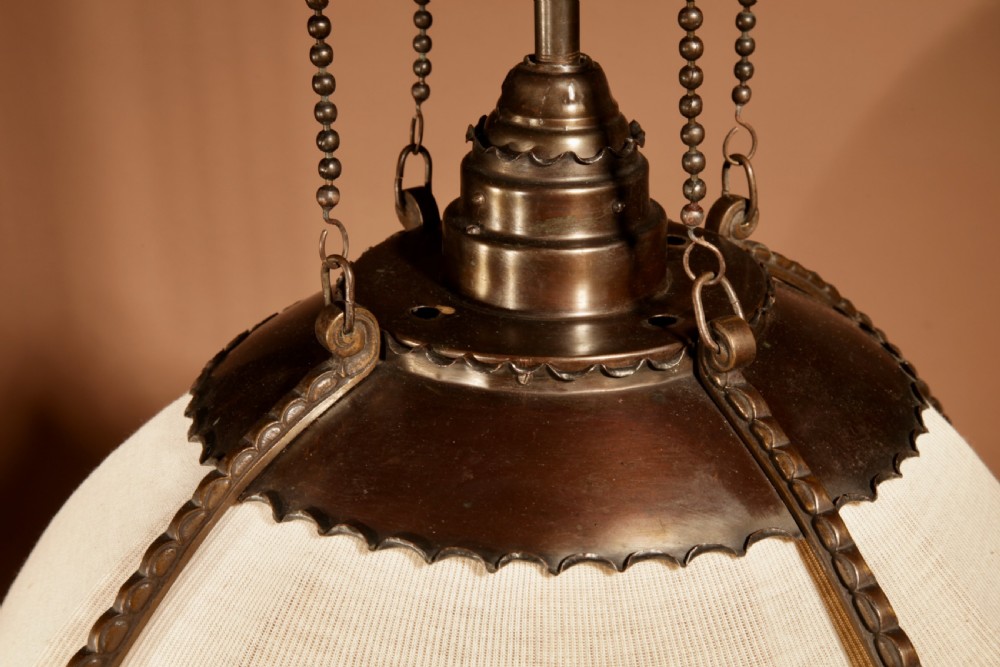 An early 20th-century Amsterdam School pendant light with a copper and brass frame, suspended by chain links, enclosing a pleated cream fabric shade. View IV
