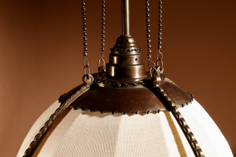 An early 20th-century Amsterdam School pendant light with a copper and brass frame, suspended by chain links, enclosing a pleated cream fabric shade. View VII