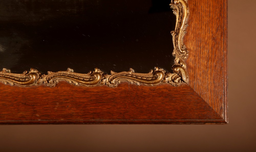 A rectangular oak wall mirror featuring a flat timber frame and a gilded gesso Rococo border surrounding the central mirror glass. View V