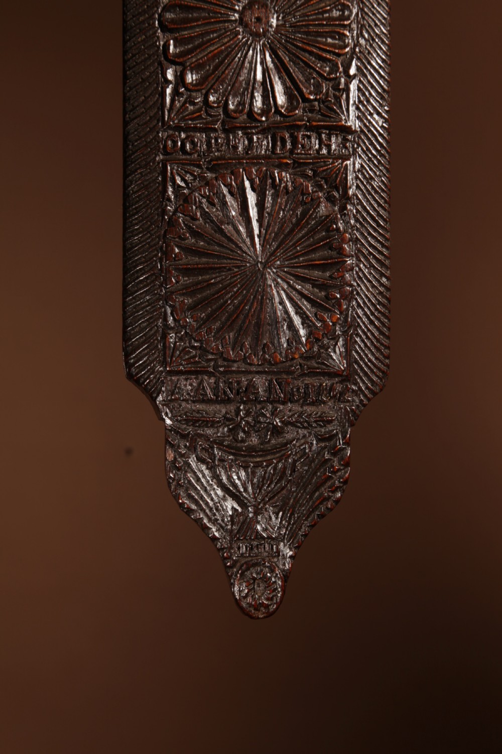 A long, narrow dark oak mangle board featuring detailed geometric chip carving, carved text bands, and a shaped top handle. View II