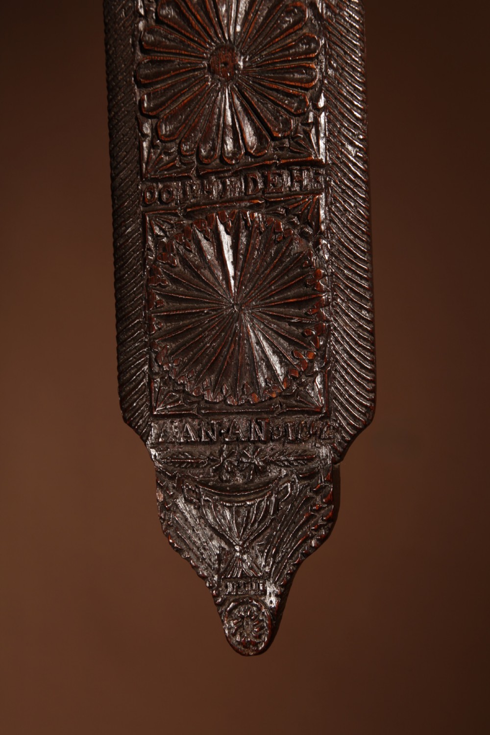 A long, narrow dark oak mangle board featuring detailed geometric chip carving, carved text bands, and a shaped top handle. View III