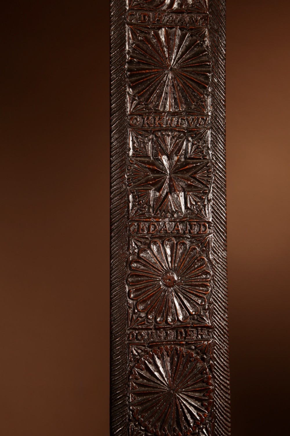 A long, narrow dark oak mangle board featuring detailed geometric chip carving, carved text bands, and a shaped top handle. View IV