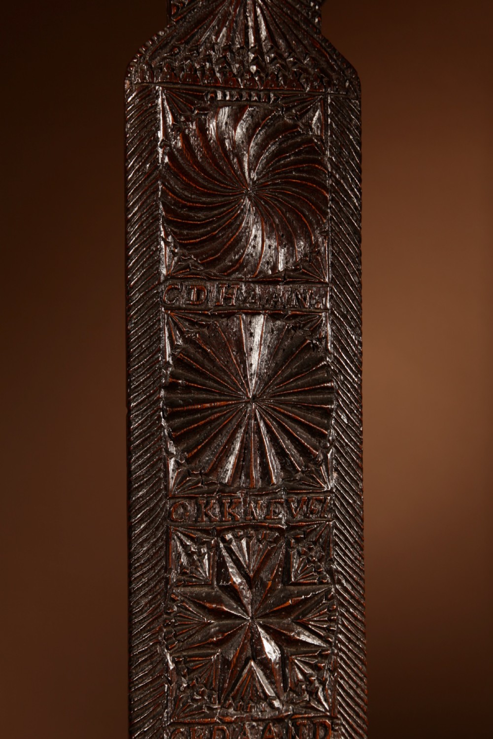 A long, narrow dark oak mangle board featuring detailed geometric chip carving, carved text bands, and a shaped top handle. View V