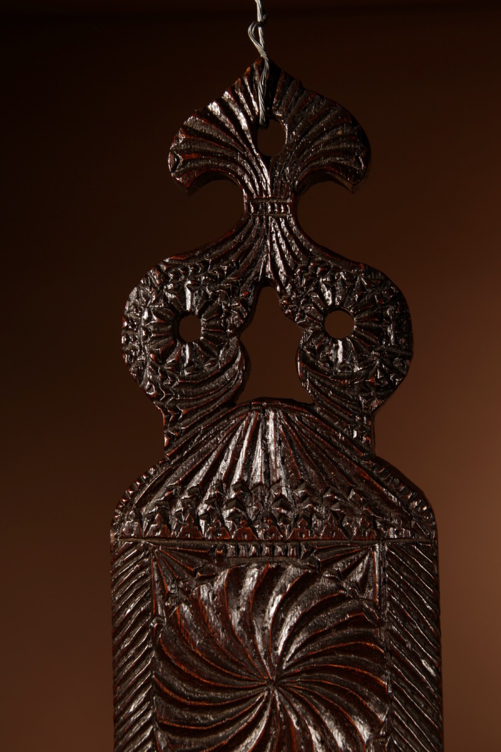 A long, narrow dark oak mangle board featuring detailed geometric chip carving, carved text bands, and a shaped top handle. View VI