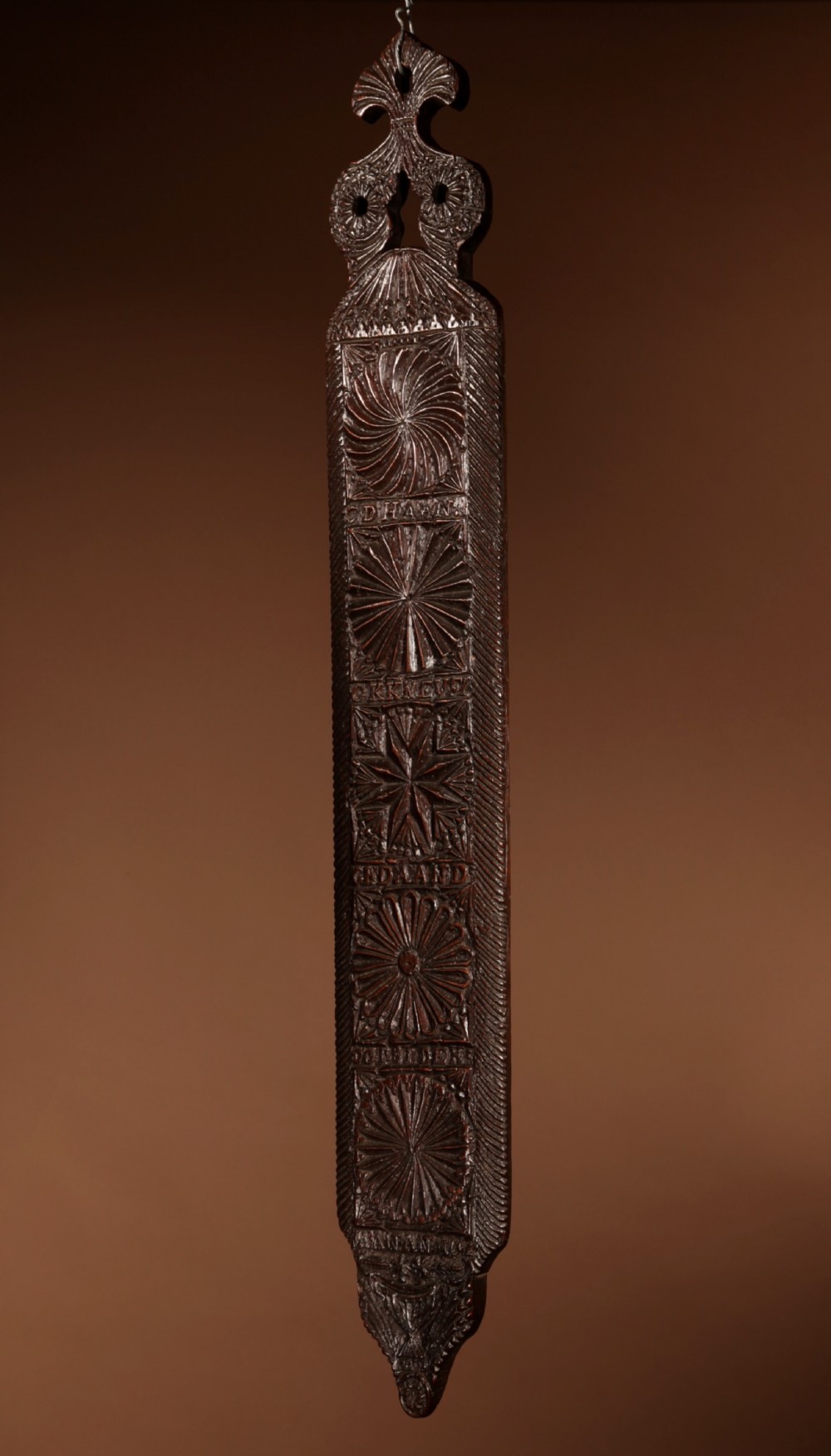 A long, narrow dark oak mangle board featuring detailed geometric chip carving, carved text bands, and a shaped top handle. View VII