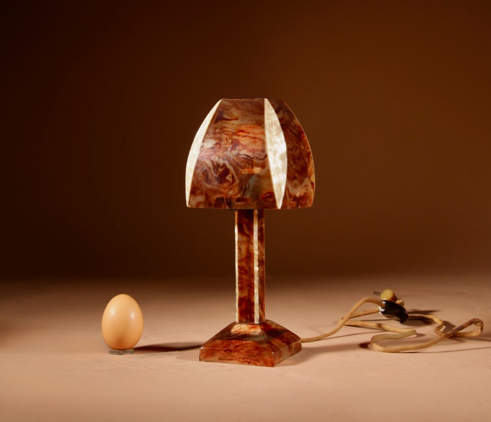 A small Art Deco table lamp made from marbled amber brown and cream celluloid with a faceted geometric shade.