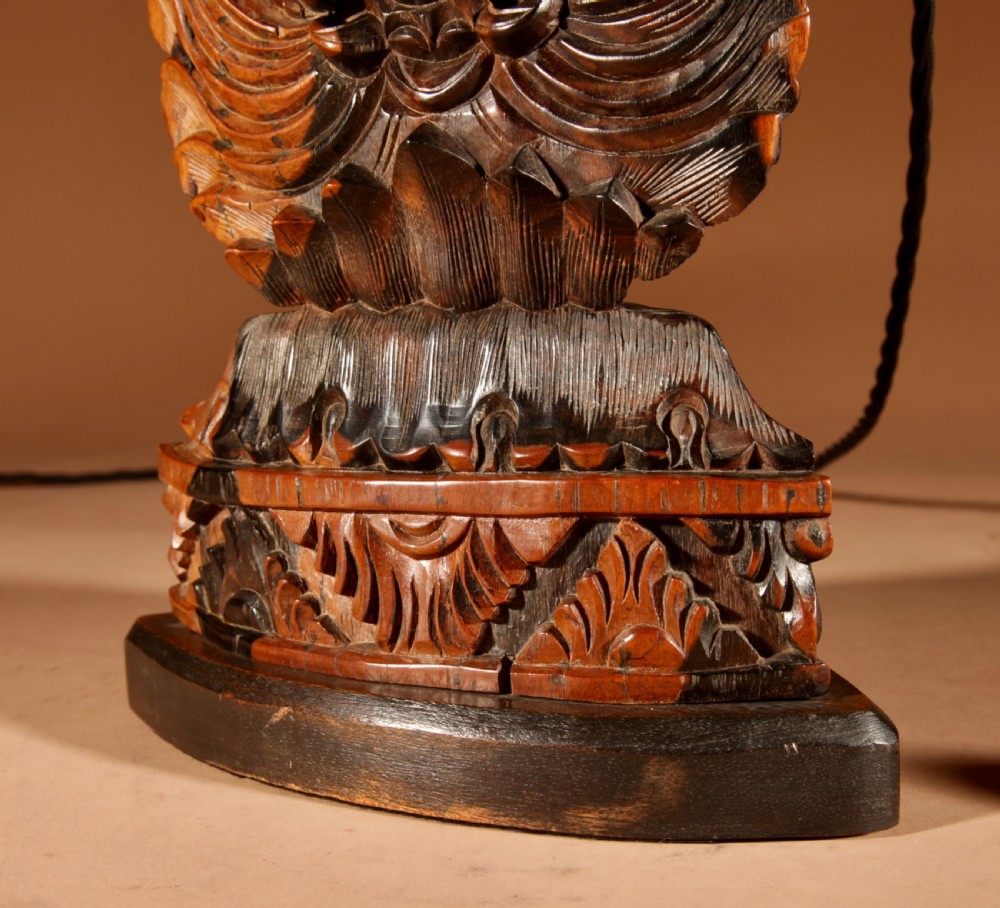 A carved dark hardwood table lamp featuring a detailed mythological mask motif and pierced lattice section, topped with a pleated beige fabric shade. View XI