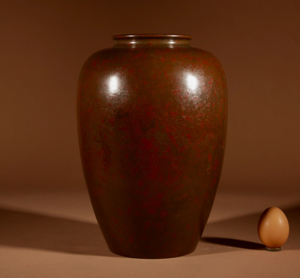 A Japanese bronze vase with a mottled red and brown patinated surface and an ovoid silhouette.