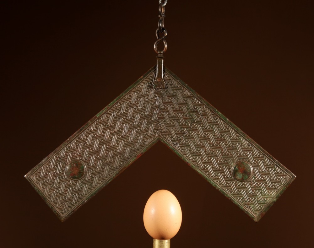 A chevron-shaped cast bronze musical chime featuring geometric relief patterns and a top suspension loop.